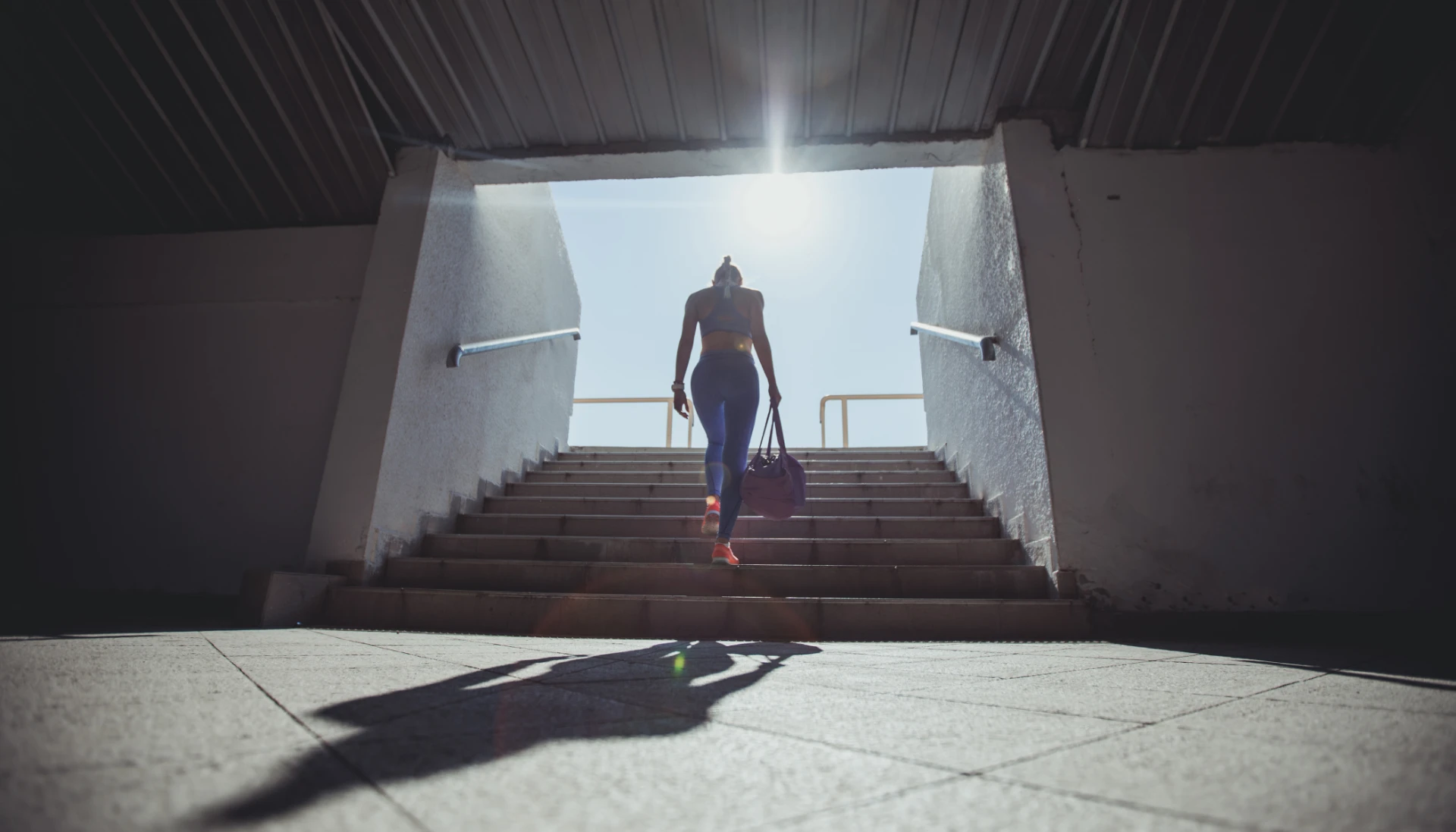 Athlete walking up stairs toward daylight, carrying a gym bag
